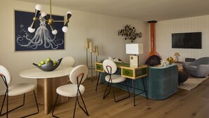 Un salon moderne avec une table de salle à manger ronde, un canapé bleu, une cheminée et un grand téléviseur.