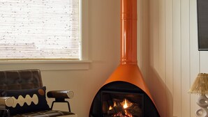 Un salon chaleureux avec une cheminée, un canapé, une table basse décorée de tournesols et une fenêtre avec des stores.