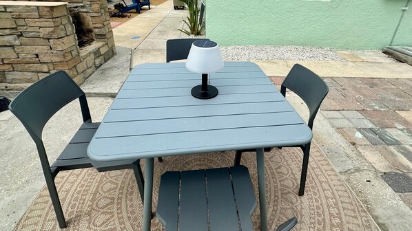 Ein quadratischer Gartentisch mit einer Solarleuchte, umgeben von vier Stühlen.