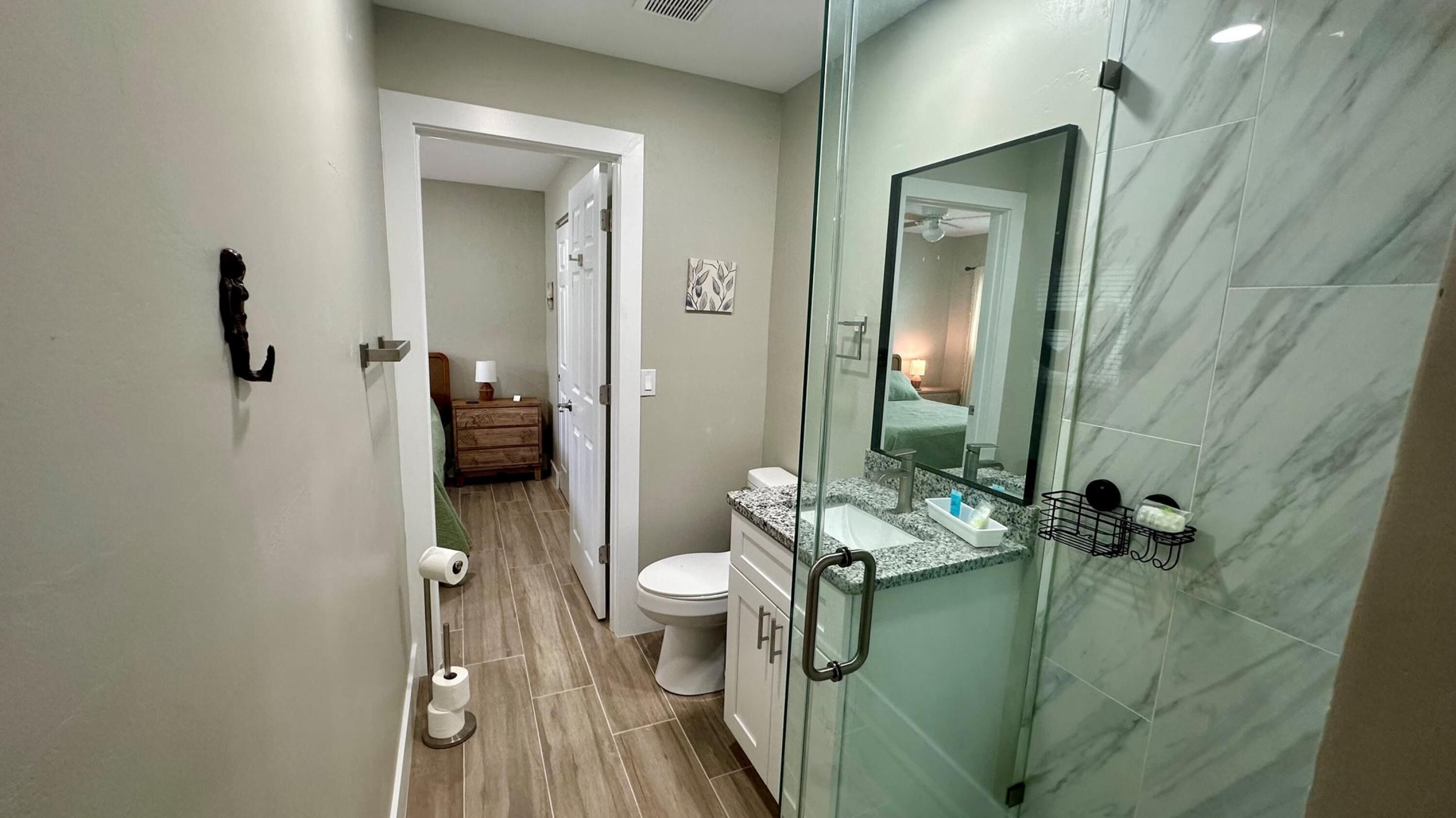 Een moderne badkamer met een glazen douchecabine, een betegelde muur van marmer en een zichtbare toilet- en wastafelruimte.