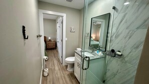 Ein modernes Badezimmer mit Duschkabine aus Glas, Marmorfliesen und einem sichtbaren Bereich für Toilette und Waschbecken.