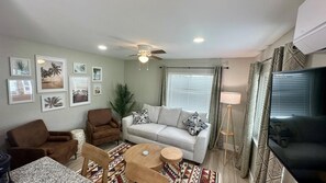 Ein Wohnzimmer mit einer Couch, Sesseln, einem Couchtisch, einem Fernseher und einem Deckenventilator.