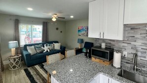 A compact living space with a kitchenette, a sofa with decorative pillows, a dining area, and a ceiling fan. - Turtle Nest 2 - Quick Walk to Beach (Fort Myers Beach)
