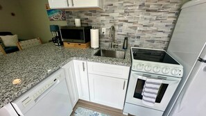A compact kitchen with white cabinets, a granite countertop, a built-in microwave, a stainless steel sink, and a stove. - Turtle Nest 2 - Quick Walk to Beach (Fort Myers Beach)