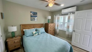 A bedroom with a bed, nightstands, a ceiling fan, a window with curtains, and an air conditioning unit. - Turtle Nest 2 - Quick Walk to Beach (Fort Myers Beach)