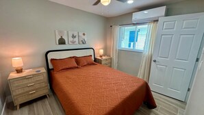 A bedroom with a bed, nightstands, a window with curtains, and a door. - Turtle Nest 4 - Quick Walk to Beach (Fort Myers Beach)