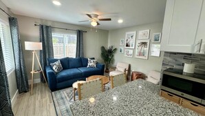 A modern living room with a blue sofa, a coffee table, and a TV. There is a ceiling fan, a floor lamp, and a potted plant. - Turtle Nest 4 - Quick Walk to Beach (Fort Myers Beach)