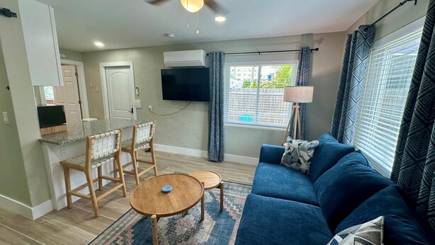 A living room with a blue sofa, a wooden coffee table, and a TV mounted on the wall. - Turtle Nest 4 - Quick Walk to Beach (Fort Myers Beach)