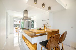 Uma cozinha moderna com uma ilha central, cadeiras de madeira e uma área de jantar visível ao fundo.