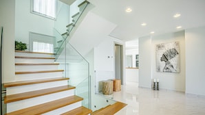 Een modern interieur met een glazen trap, houten treden en een marmeren vloer.