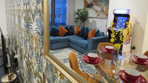 Una sala de estar con un sofá azul, una mesa de comedor con vajilla roja y blanca, y un espejo grande que refleja la habitación.