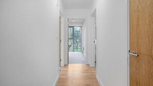 Un pasillo estrecho con suelo de madera y paredes blancas, que conduce a una puerta con manija metálica.