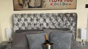 A neatly made bed with a heart-shaped arrangement of rose petals and a bottle of champagne in a bucket. - Stunning 1-Bed Cottage in Halifax (Halifax)
