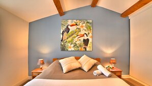 A bedroom with a large bed, two bedside lamps, a wooden headboard, and a tropical-themed painting on the wall. - Les coutures by Interhome (Ile d'Oléron)