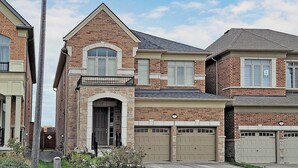 A two-story house with a brick facade, a central entrance with a door, and two garage doors. - Charming 2- Bedroom With Free Parking Space (Whitby)