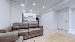 A modern living room with a leather sofa, a wooden coffee table, and a kitchen in the background. - Charming 2- Bedroom With Free Parking Space (Whitby)