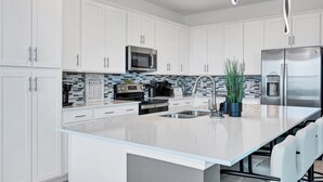 Een moderne keuken met witte kasten, een roestvrijstalen koelkast, een magnetron en een groot eiland met een spoelbak.