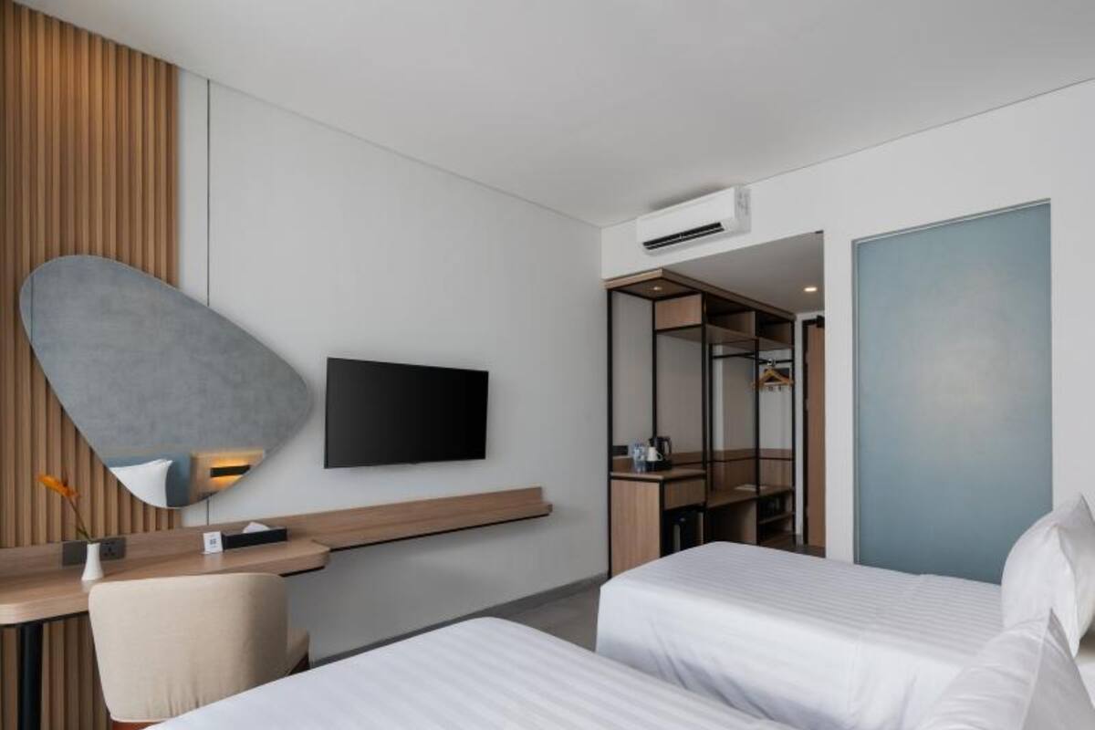 A modern hotel room with a large bed, a desk with a chair, a flat-screen TV mounted on the wall, and a walk-in closet.