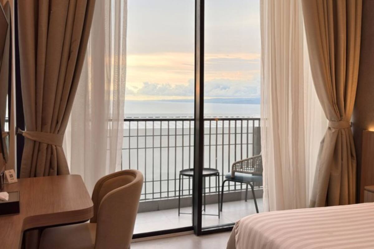 A hotel room with a large window, a bed, a desk, and a chair.