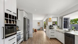 A modern kitchen with white cabinetry, a stainless steel refrigerator, a built-in oven, and a dishwasher. - Luxury coastal retreat only 250m from the beach! (Tweed)