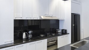 A modern kitchen with white cabinets, a black countertop, a stainless steel sink, a black refrigerator, and a built-in oven. - Villa Bebek Best Eat Street location in Seminyak,  (Seminyak)