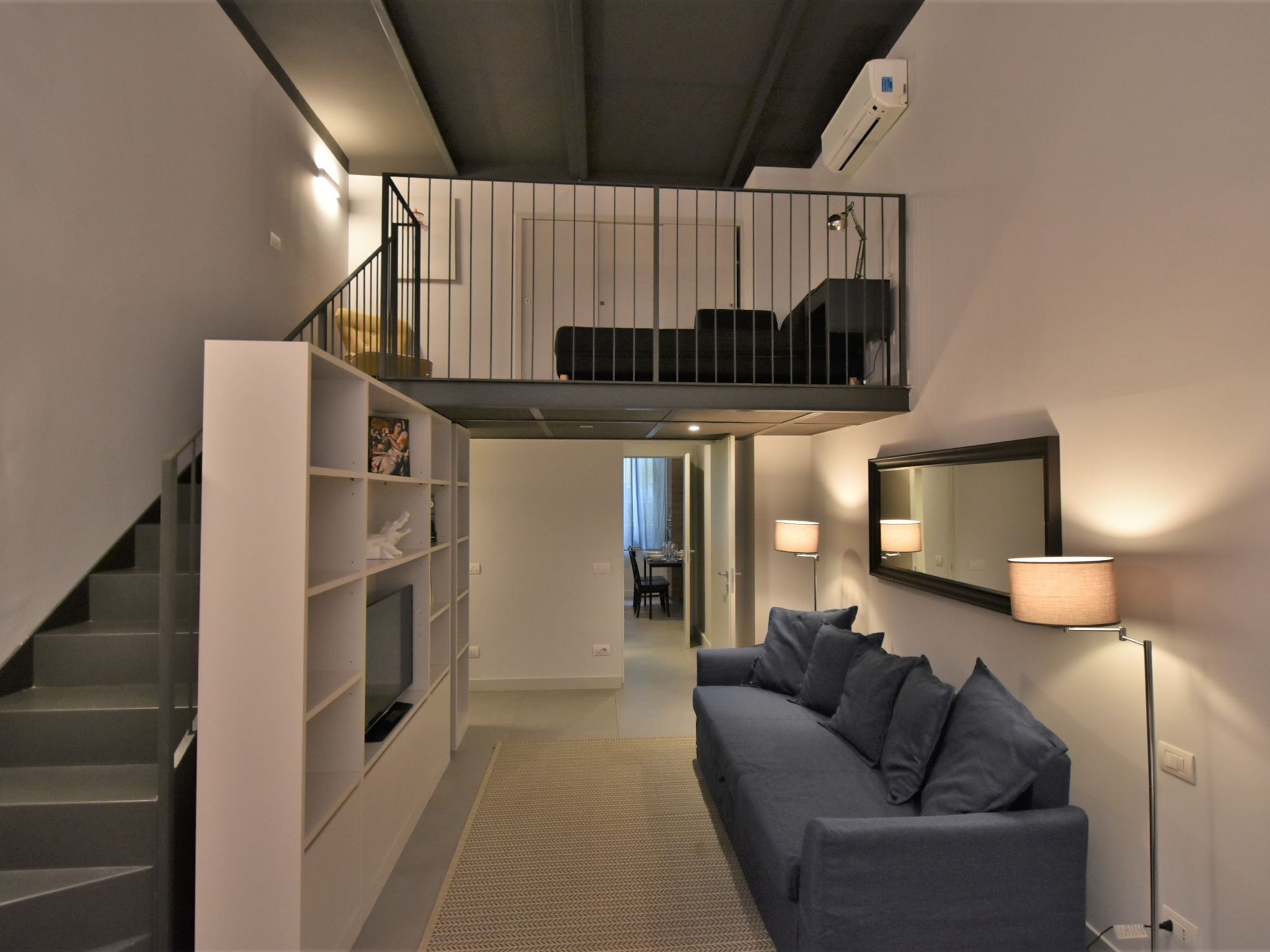 Ein moderner Wohnraum mit Treppe, Sofa, Bücherregal, Essbereich und Balkon.
