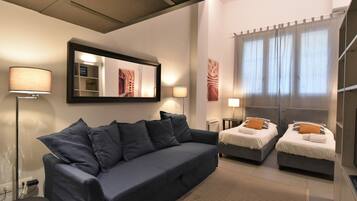 Ein modernes Hotelzimmer mit einem dunkelblauen Sofa, zwei Einzelbetten, einem großen Spiegel und Blick auf die Stadt durch transparente Vorhänge.