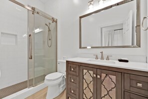 Une salle de bain moderne avec une douche à parois de verre, des toilettes blanches et un meuble-lavabo doté d’un grand miroir.