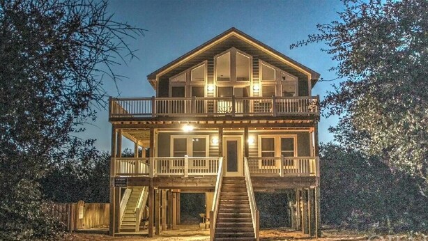A two-story wooden cabin with a balcony on the upper level, surrounded by trees.