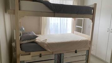 Uma cama beliche com gavetas para guardar objetos, uma luminária de cabeceira e uma janela com cortinas.