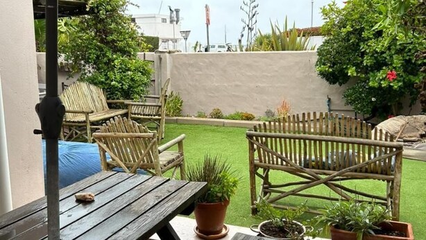 An outdoor patio with a wooden table and chairs, a covered area with a mesh canopy, and potted plants. - Room-cozy Crner Kitehouse (Langebaan)