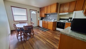 A compact kitchen with wooden cabinets, a dining table with chairs, a built-in oven, and a refrigerator.