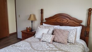 A neatly made bed with a patterned bedspread and several pillows, a wooden nightstand with a lamp, and a wooden door in the background.