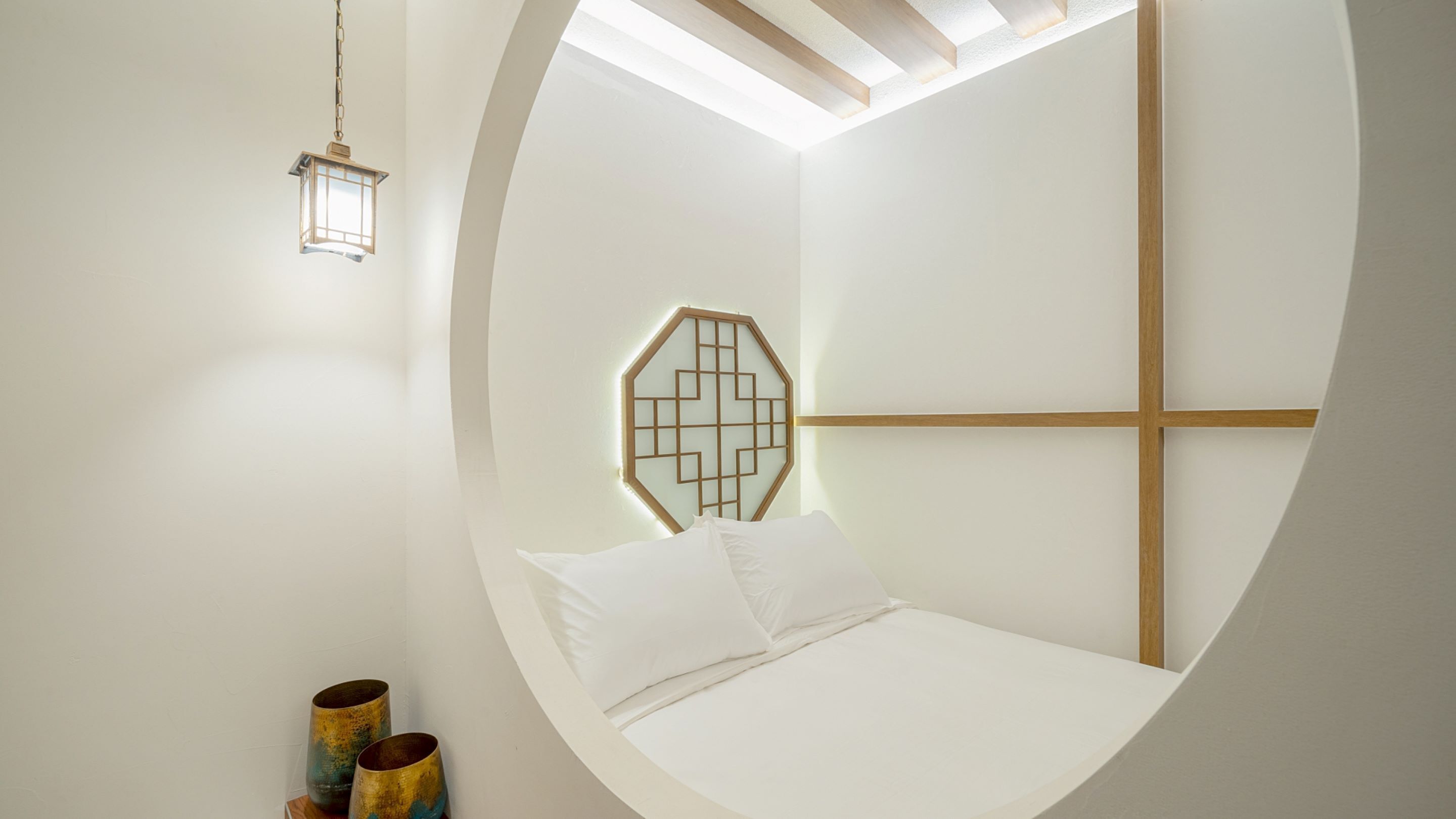 A circular room with a bed, a hanging lantern, and a geometric wall decoration.