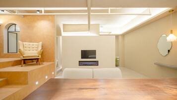 A modern living room with a sofa, a flat-screen TV, a fireplace, and a dining table.