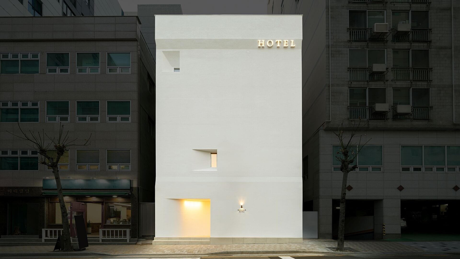 Fachada moderna de hotel con un llamativo letrero que dice 'HOTEL', una entrada acogedora y un pequeño letrero iluminado que indica el nombre del hotel.