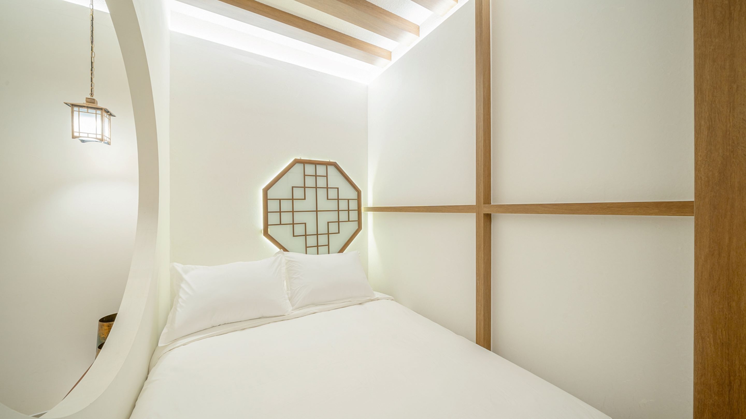 Un dormitorio con cama con dosel, decoración geométrica en la pared y una lámpara colgante.