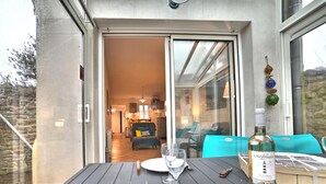 Ein Esstisch ist gedeckt mit einer Weinflasche, einem Glas, einem Teller und Besteck auf einem Balkon mit Blick ins Innere.