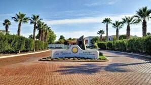 Der Eingang eines Resorts mit Palmen und einem gepflasterten Weg.