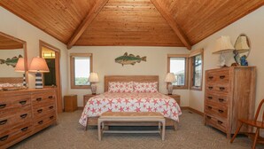 Une chambre avec un plafond en bois, un lit recouvert d’une couvre-lit à motifs d’étoiles, deux lampes de chevet, une commode, un miroir et un décor mural représentant des poissons.