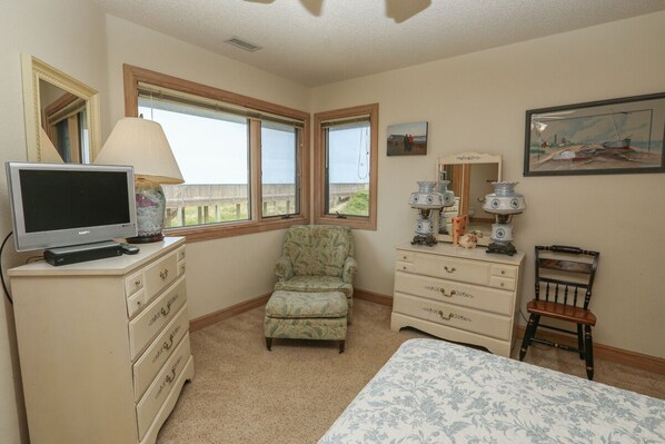 A bedroom with a bed, a television, a chair, a dresser, and a window with a view of a wooden deck.