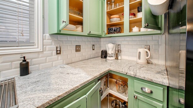 Een keuken met groene kastjes, een granieten aanrechtblad en diverse apparaten, waaronder een koffiezetapparaat en een broodrooster.