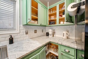 Une cuisine avec des meubles de couleur verte, un plan de travail en granit et divers appareils, notamment une machine à café et un grille-pain.