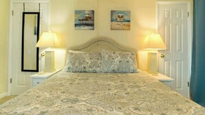 Quarto com uma cama grande, duas luminárias de apoio, uma cabeceira e dois quadros na parede.
