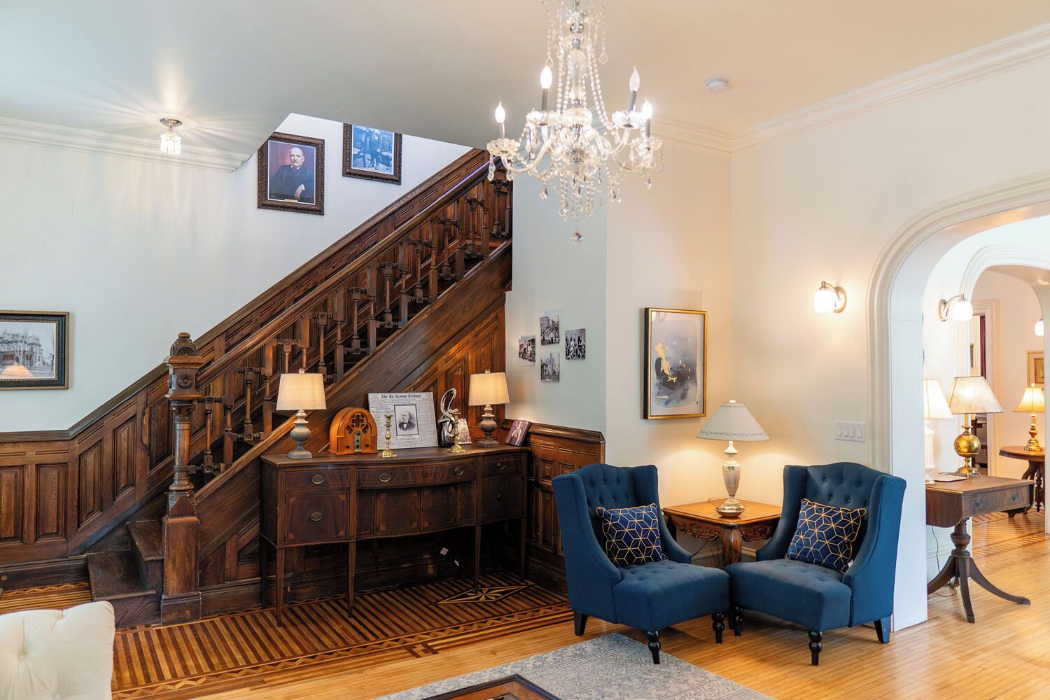 Un magnifique escalier en bois avec des rampes, un lustre et des tableaux encadrés qui ornent les murs.