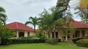 A two-story building with a red-tiled roof, surrounded by well-maintained lawns and tropical plants. - Beautiful Bungalow With Shared Outdoor Pool (Cha-am)