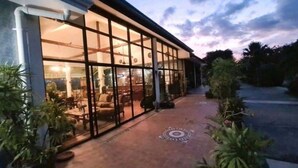 A modern building with large glass windows and a paved entrance area. - Beautiful Bungalow With Shared Outdoor Pool (Cha-am)