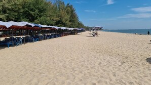 A beach with rows of sun loungers and umbrellas, a clear sky, and a calm sea. - Beautiful Bungalow With Shared Outdoor Pool (Cha-am)