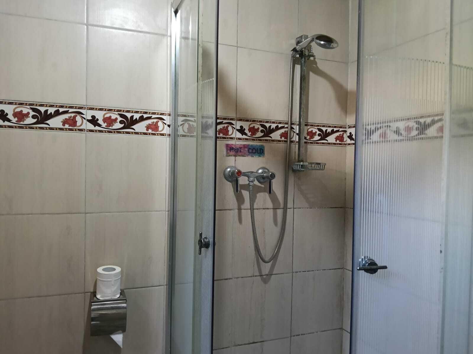 A shower area with a glass door, a toilet paper holder, and decorative tiles.