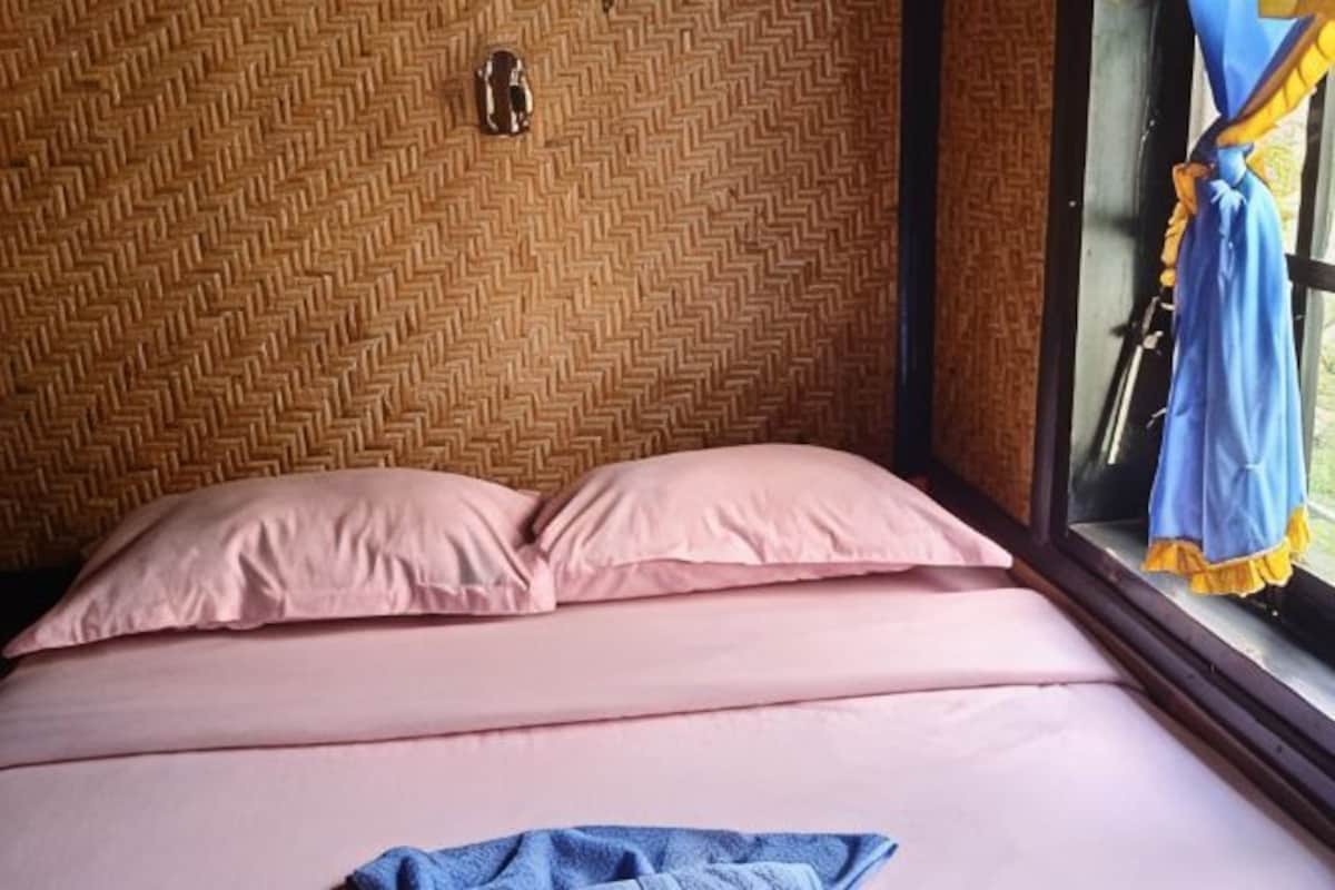 A bed with pink bedding, a blue towel, and a window with a curtain.